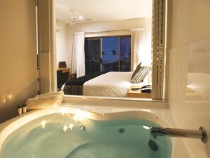 Una habitación de hotel con una cama grande, una ventana con cortinas, una mesita de noche con lámpara y una bañera con agua.