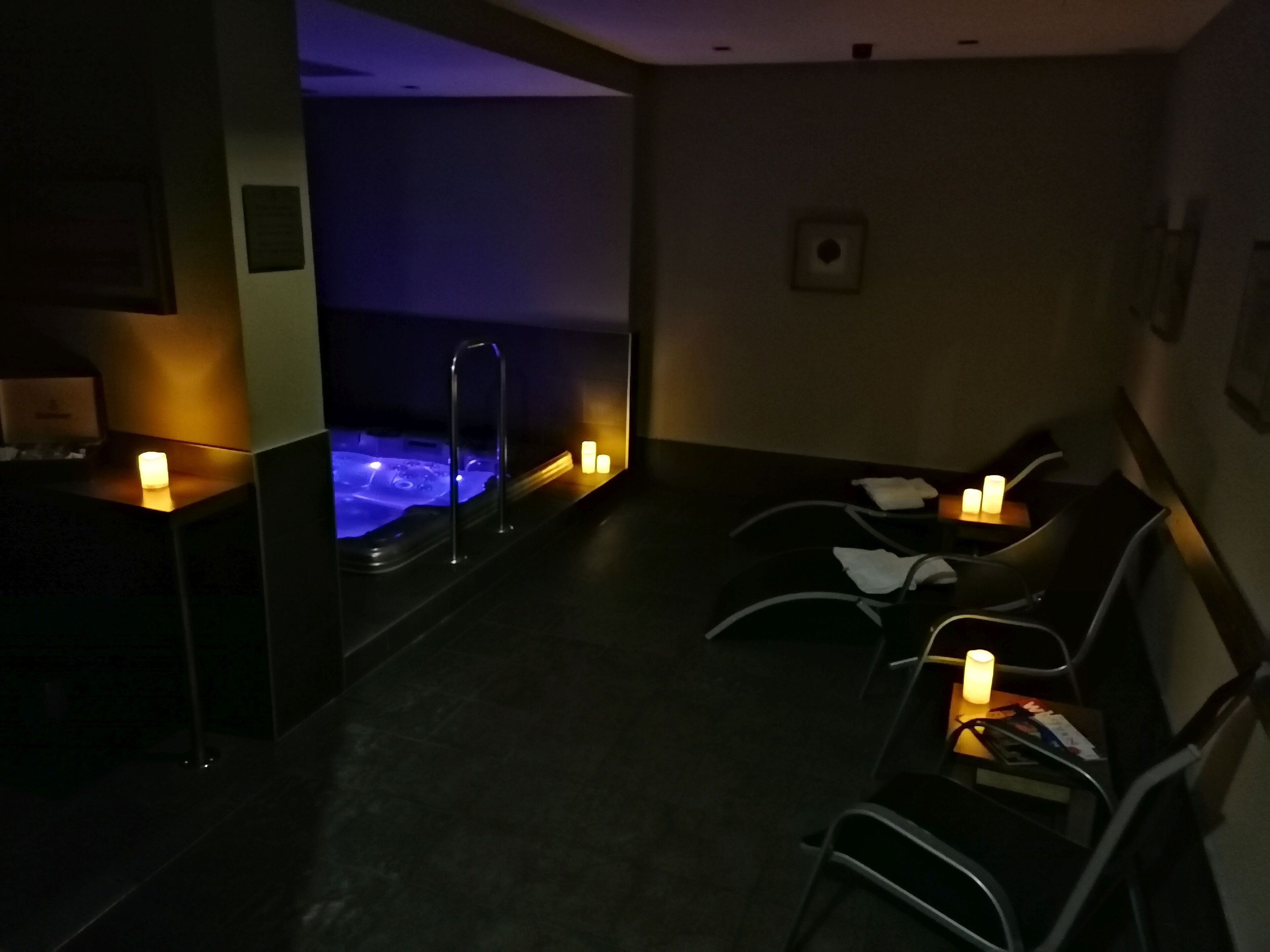 Zona de spa tenuemente iluminada con un jacuzzi, velas y asientos.