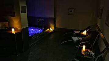 Zona de spa tenuemente iluminada con un jacuzzi, velas y asientos.