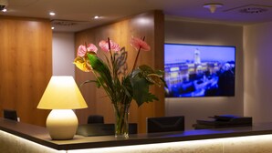 A reception desk with a lamp, a vase of flowers, and a television displaying a cityscape. - Hotel Castle Garden (Budapest)