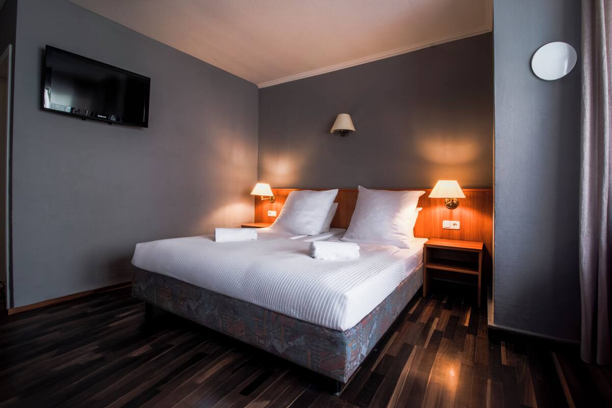 A hotel room with a bed, two bedside lamps, a flat-screen TV, and a wall-mounted light fixture.
