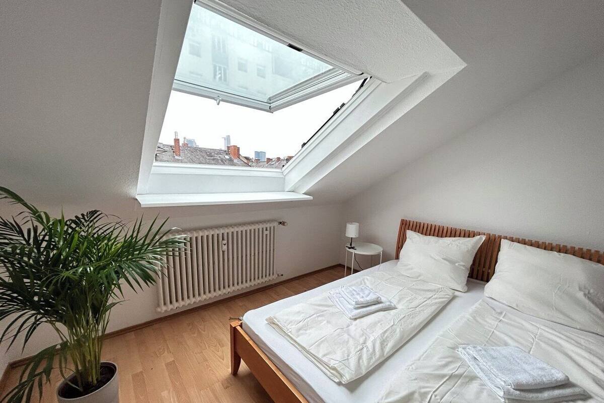 A bedroom with a skylight, a radiator, a bedside table, a lamp, and a potted plant.