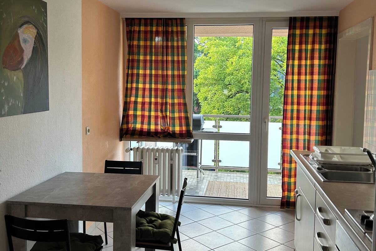 A dining area with a table and chairs, a kitchen with a sink and cabinets, and a view through a glass door to an outdoor area.