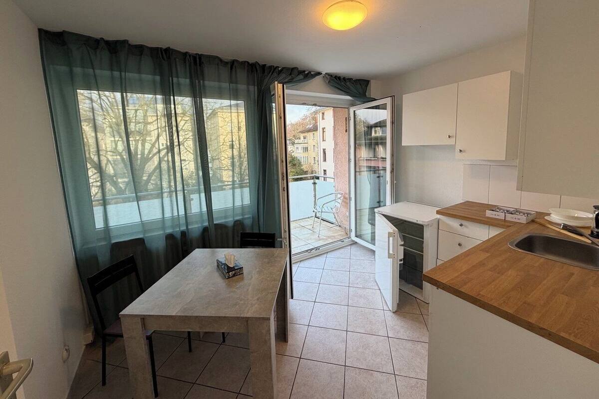 A compact kitchen with a dining table, a sink, and a view of the outside balcony.