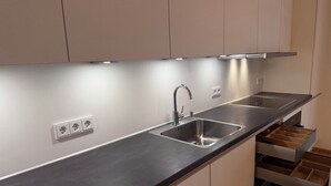 A modern kitchen with a stainless steel sink, a built-in oven, and a countertop with integrated lighting.