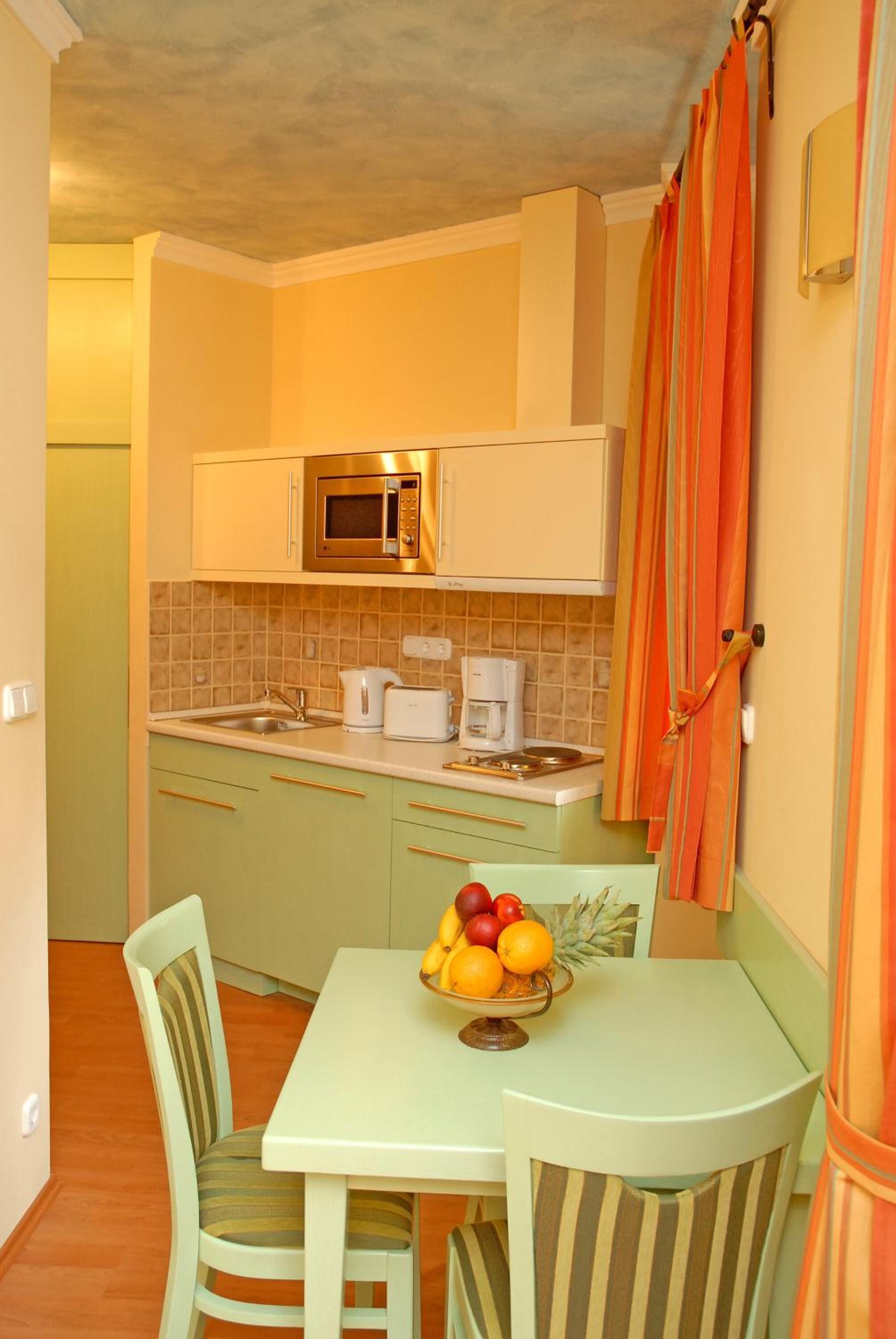 Una cocina compacta con microondas, cafetera y un frutero sobre la mesa.