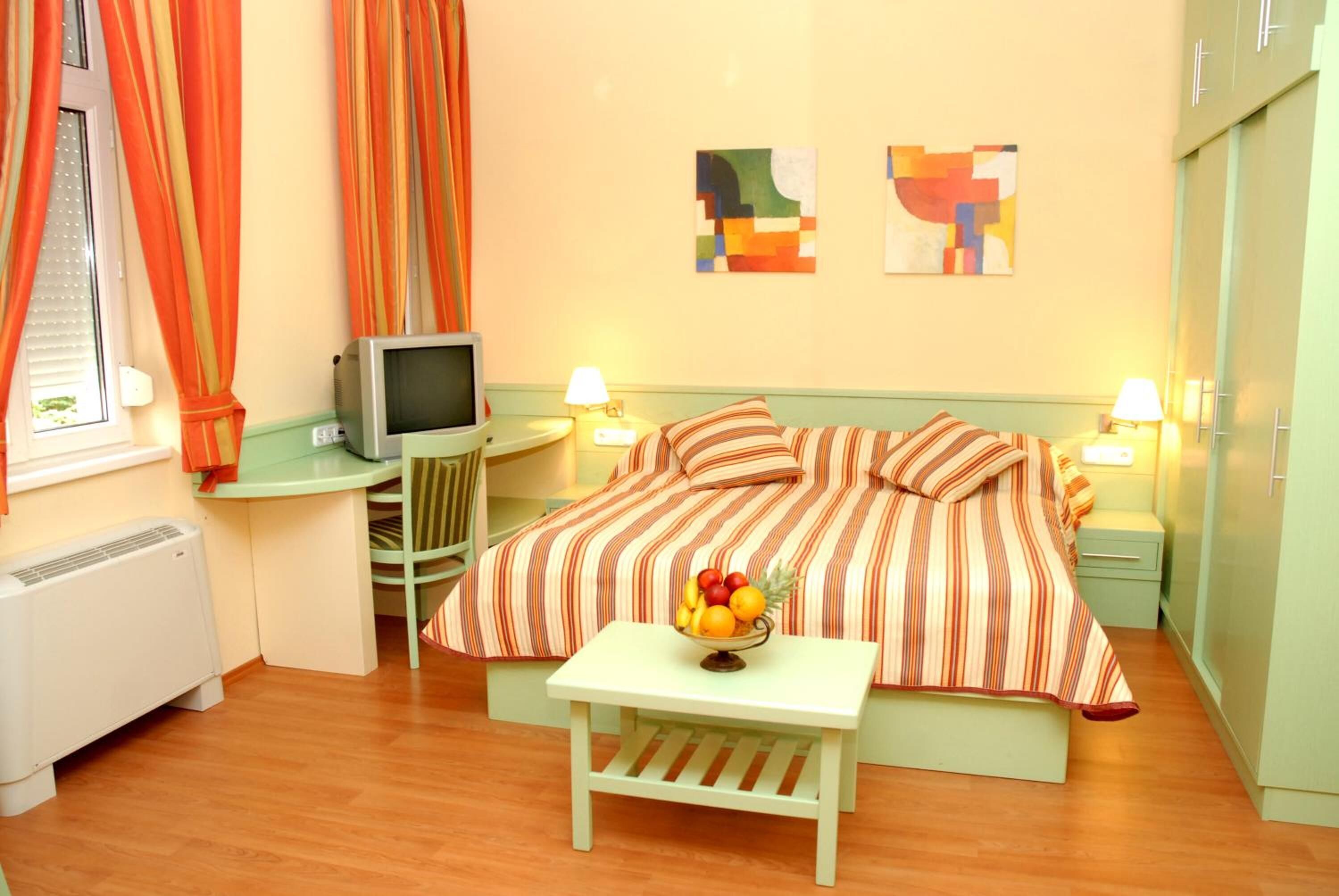 Habitación de hotel con una cama, televisión, una mesita con fruta y dos lámparas.