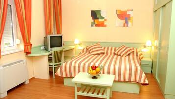 Habitación de hotel con una cama, televisión, una mesita con fruta y dos lámparas.