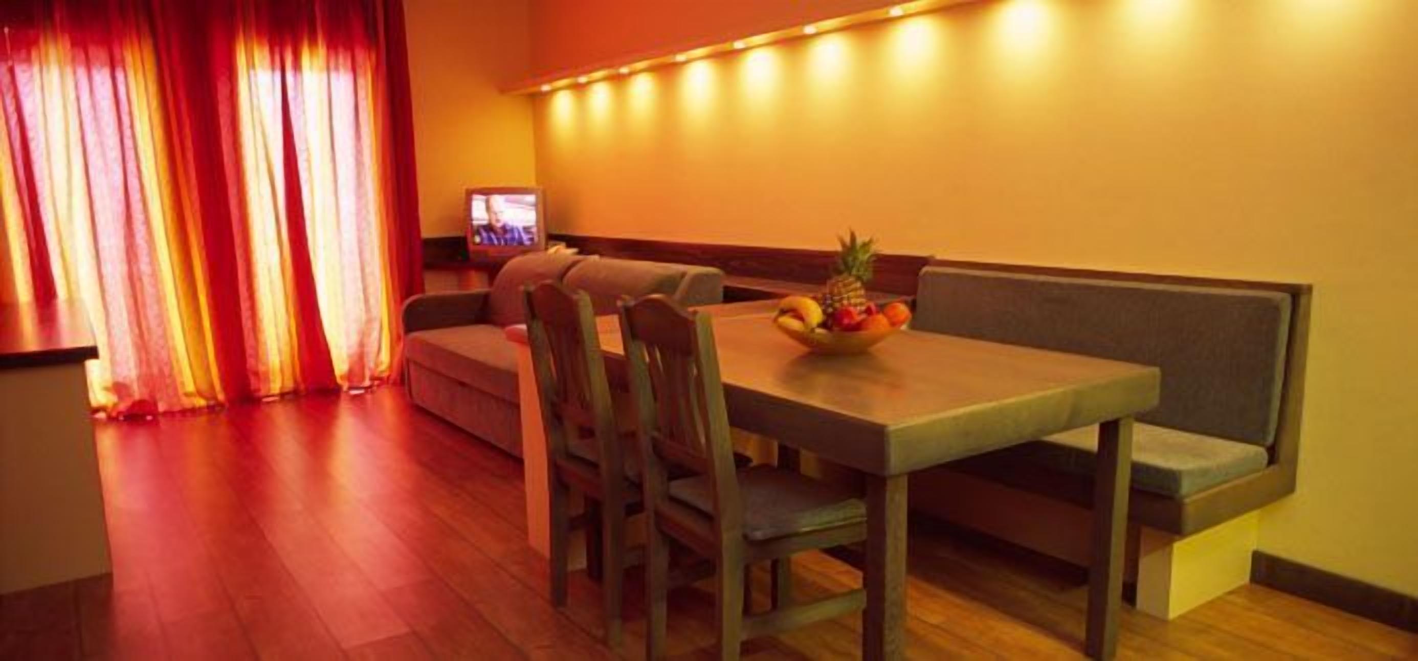 Un comedor con una mesa de madera, asientos acolchados y un frutero sobre la mesa.