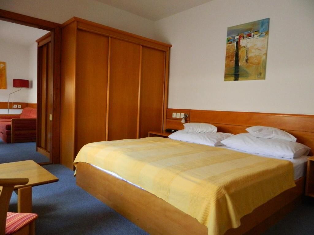 Una habitación de hotel con una cama, un armario de madera, una mesita de noche y un cuadro en la pared.