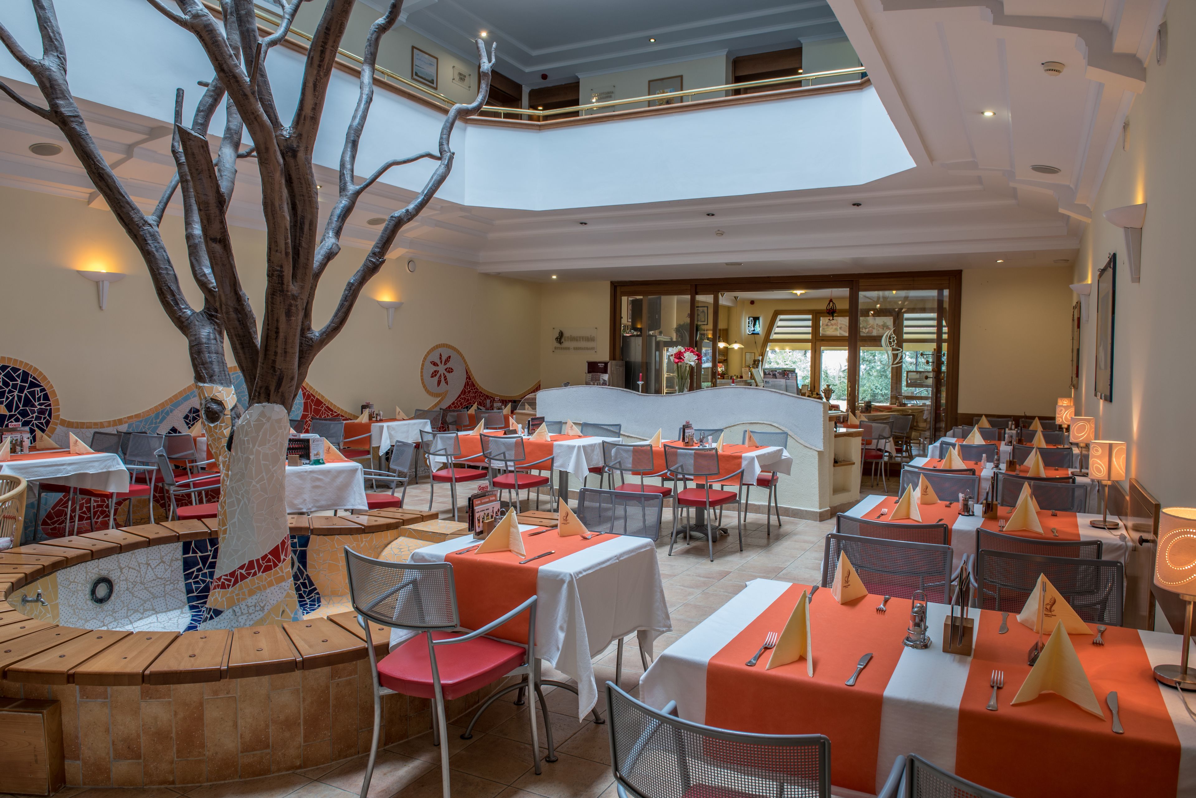Un restaurante con varias mesas, sillas y un árbol decorativo.