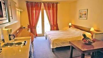 Una habitación de hotel con una cama, un escritorio con cafetera y un frutero en la mesita de noche.