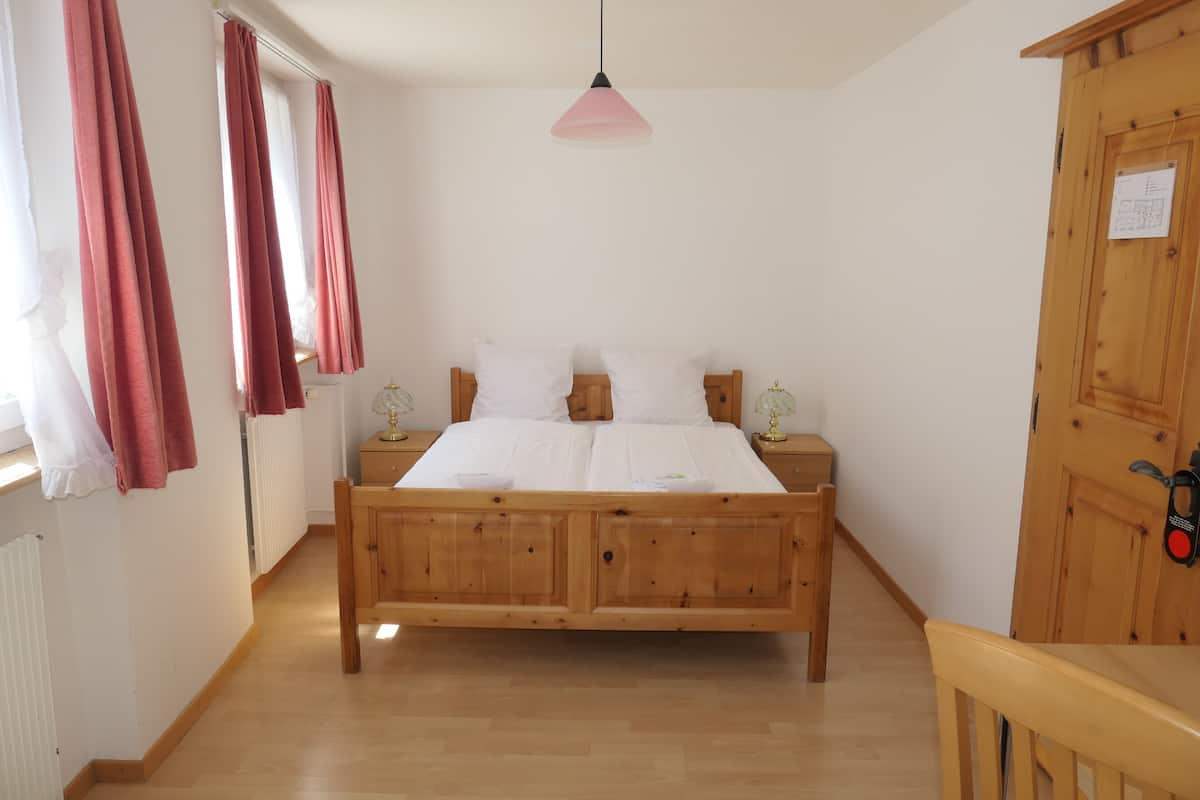 Quarto com cama de madeira, duas mesas de cabeceira, guarda-roupa de madeira e luminária pendente rosa.