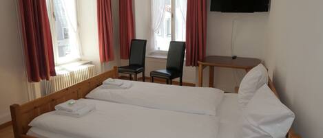 A bedroom with a wooden bed, two chairs, a small table, and a TV on the wall.