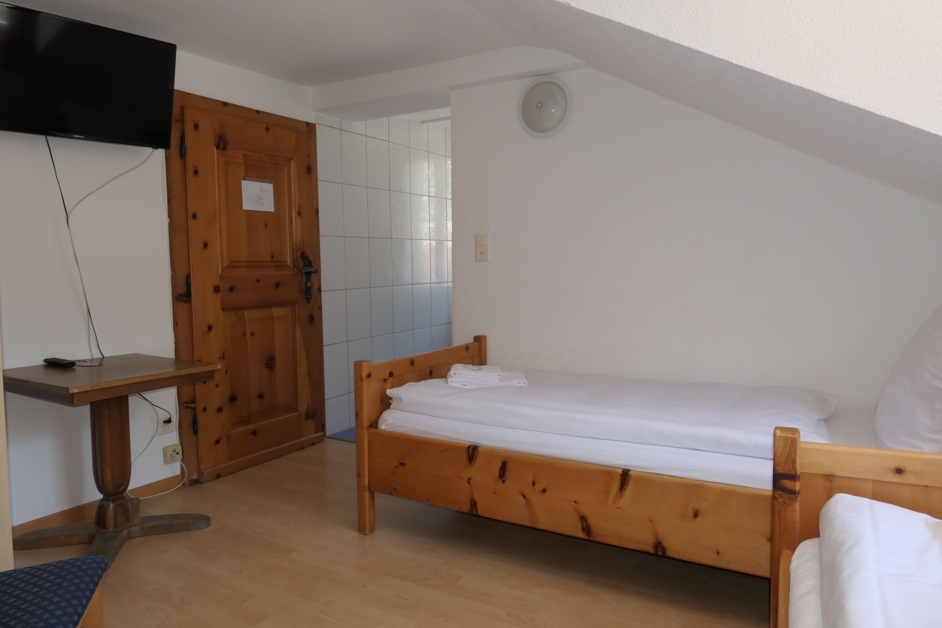 A bedroom with a wooden bed, a small desk, and a television mounted on the wall.
