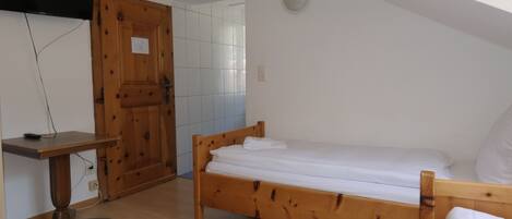 A bedroom with a wooden bed, a small desk, and a television mounted on the wall.