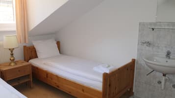 A single bed with a wooden frame, a bedside table with a lamp, and a bathroom with a sink and mirror.