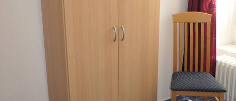 Una habitación con un armario de madera, una silla y un radiador.