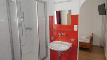 A bathroom with a glass shower enclosure, a white sink, and a red accent wall.