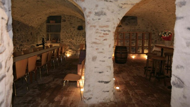 Un interior con paredes de piedra, una zona de bar con taburetes y un barril de madera.