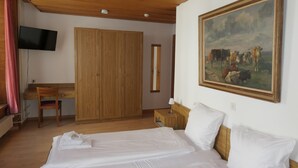 Un dormitorio con cama, escritorio, silla, armario, televisor y un cuadro de vacas.