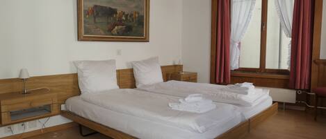A bedroom with a large bed, wooden headboard, a painting on the wall, and a window with curtains.