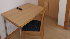 Una habitación pequeña con una mesa de madera, una silla, un televisor montado en la pared y un armario de madera.