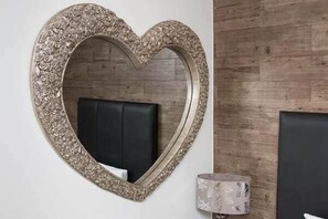 A heart-shaped mirror with an ornate frame, a black upholstered headboard, and a wooden wall. - The Arthington Guest House (Blackpool)