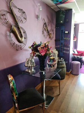 A room with a purple wall, a glass table with a vase of flowers, a chair, and a decorative metal sculpture. - The Arthington Guest House (Blackpool)
