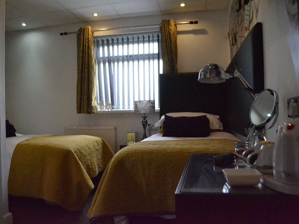 A hotel room with two beds, a desk with a lamp, a mirror, and a window with curtains.