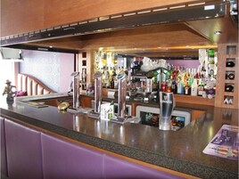 Uma área de bar com bancada de granito, diversas ferramentas de bar e uma variedade de garrafas de bebidas alcoólicas.
