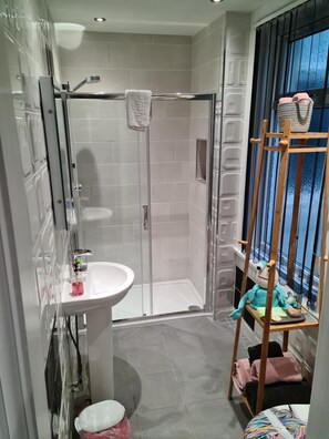 A modern bathroom with a glass shower enclosure, a white sink, and a wooden shelf with towels and a plush toy. - The Arthington Guest House (Blackpool)