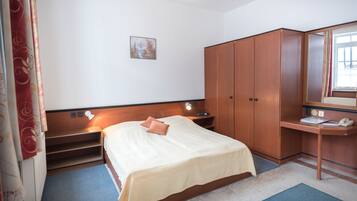 Ein Hotelzimmer mit Bett, Schreibtisch, Kleiderschrank, einem Gemälde an der Wand und einem fenster mit Vorhängen.