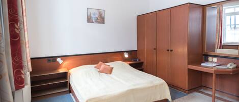 A hotel room with a bed, a desk, a wardrobe, a painting on the wall, and a window with curtains.