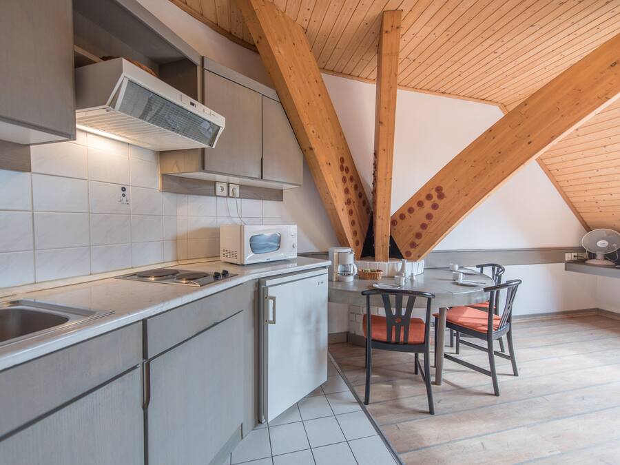 Cozinha moderna com micro-ondas, fogão e pia. Há uma mesa de jantar com cadeiras e estrutura de teto em madeira.