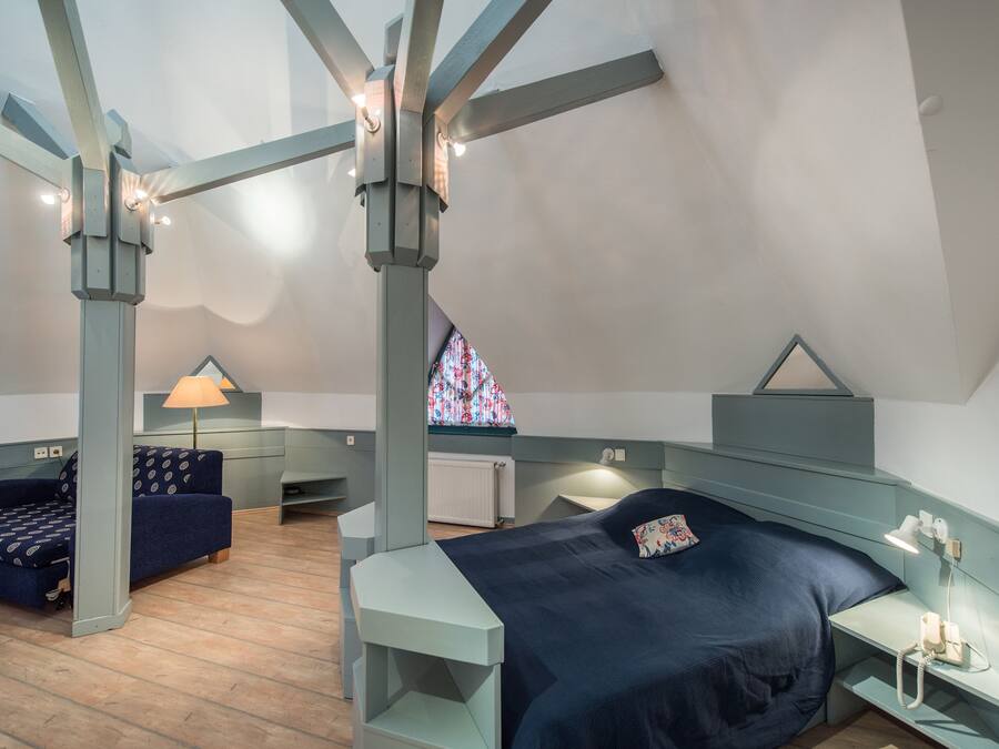 Un dormitorio con cama, escritorio, silla y ventana con diseño de vitral.