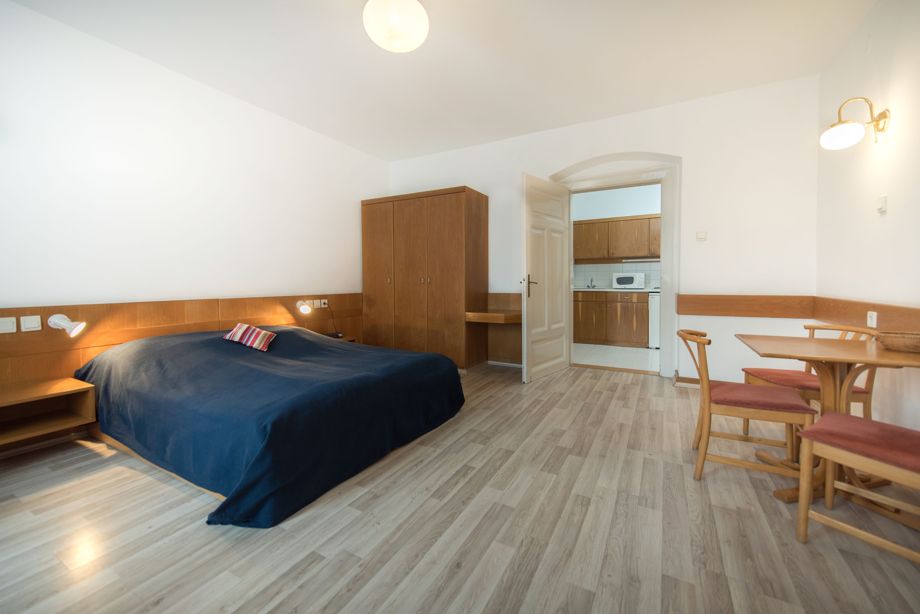 A bedroom with a bed, wooden wardrobe, and a small kitchenette.