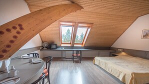 Une pièce avec un plafond en pente, une table à manger avec des chaises, un lit avec une tête de lit et une fenêtre donnant sur des arbres.