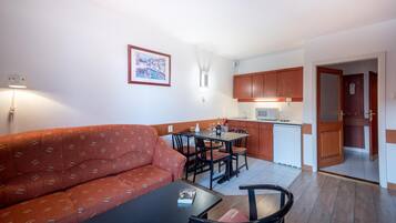 A compact living space with a sofa, dining table, chairs, a kitchenette, and a small kitchen area.