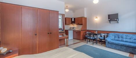 A bedroom with a bed, a sofa, a desk, and a kitchenette.