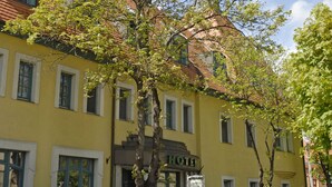 Un bâtiment jaune avec une enseigne sur laquelle on peut lire « HÔTEL » et un arbre devant.