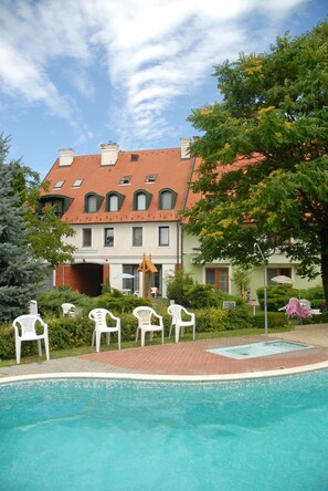 Un bâtiment avec un toit recouvert de tuiles rouges, une piscine et des chaises en plastique blanches.