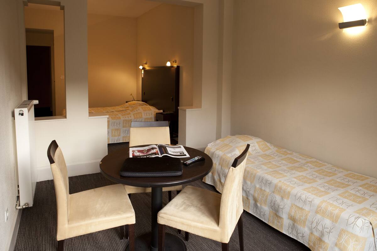 Una habitación de hotel pequeña con una cama individual, un escritorio con dos sillas, un espejo y una lámpara fijada a la pared.