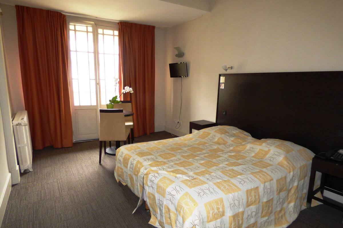 Una habitación de hotel con cama, escritorio, silla, radiador y televisor.
