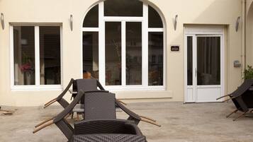 An outdoor seating area with wicker chairs and a table, a large arched window, and a door with a sign.