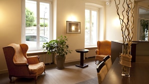 A room with a large window, a potted plant, a chair, a table, and a vase with a plant. - Le Beausejour (Plombieres-les-Bains)