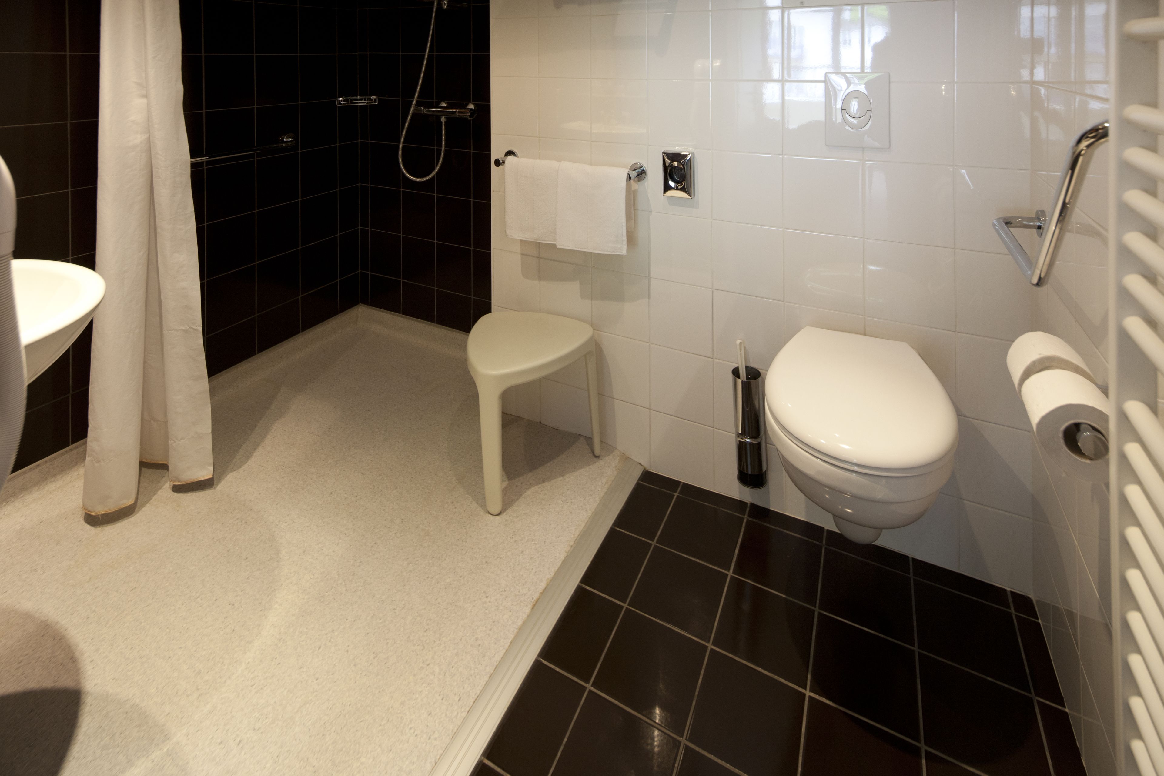 A bathroom with a white toilet, a small white stool, a shower area, and a towel rack.
