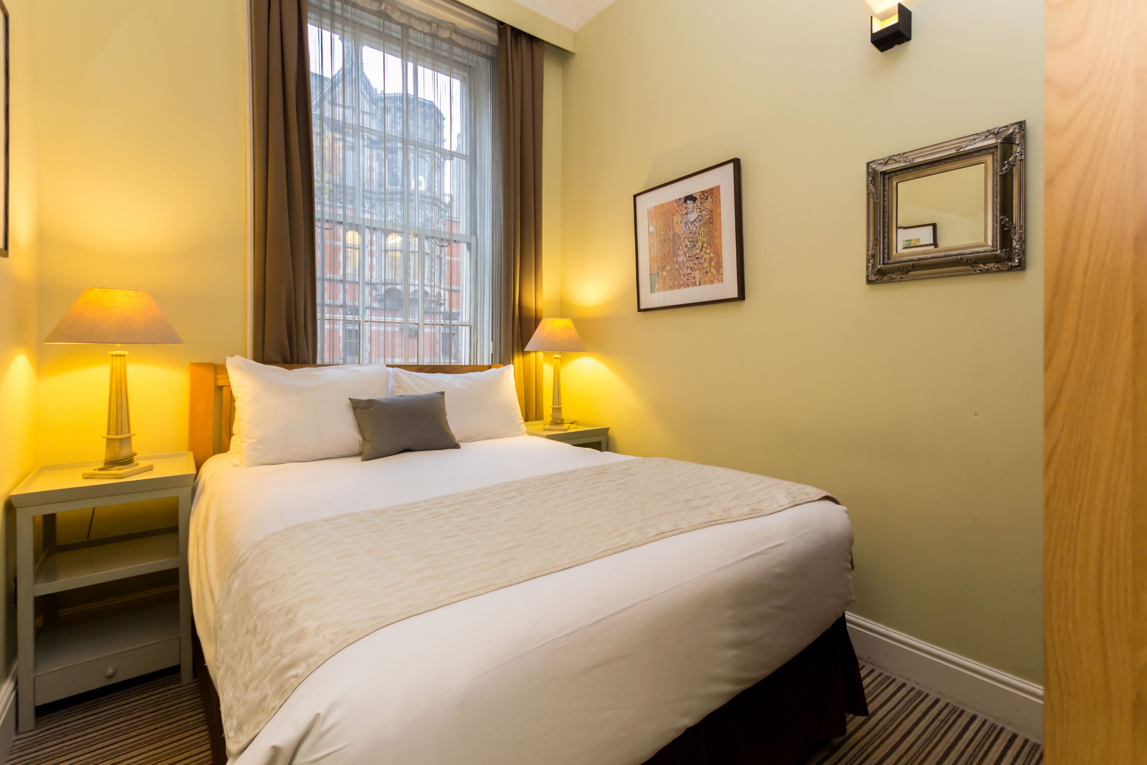 A hotel room with a large bed, two bedside lamps, a framed picture on the wall, and a window with curtains.