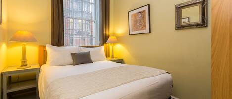 A hotel room with a large bed, two bedside lamps, a framed picture on the wall, and a window with curtains.