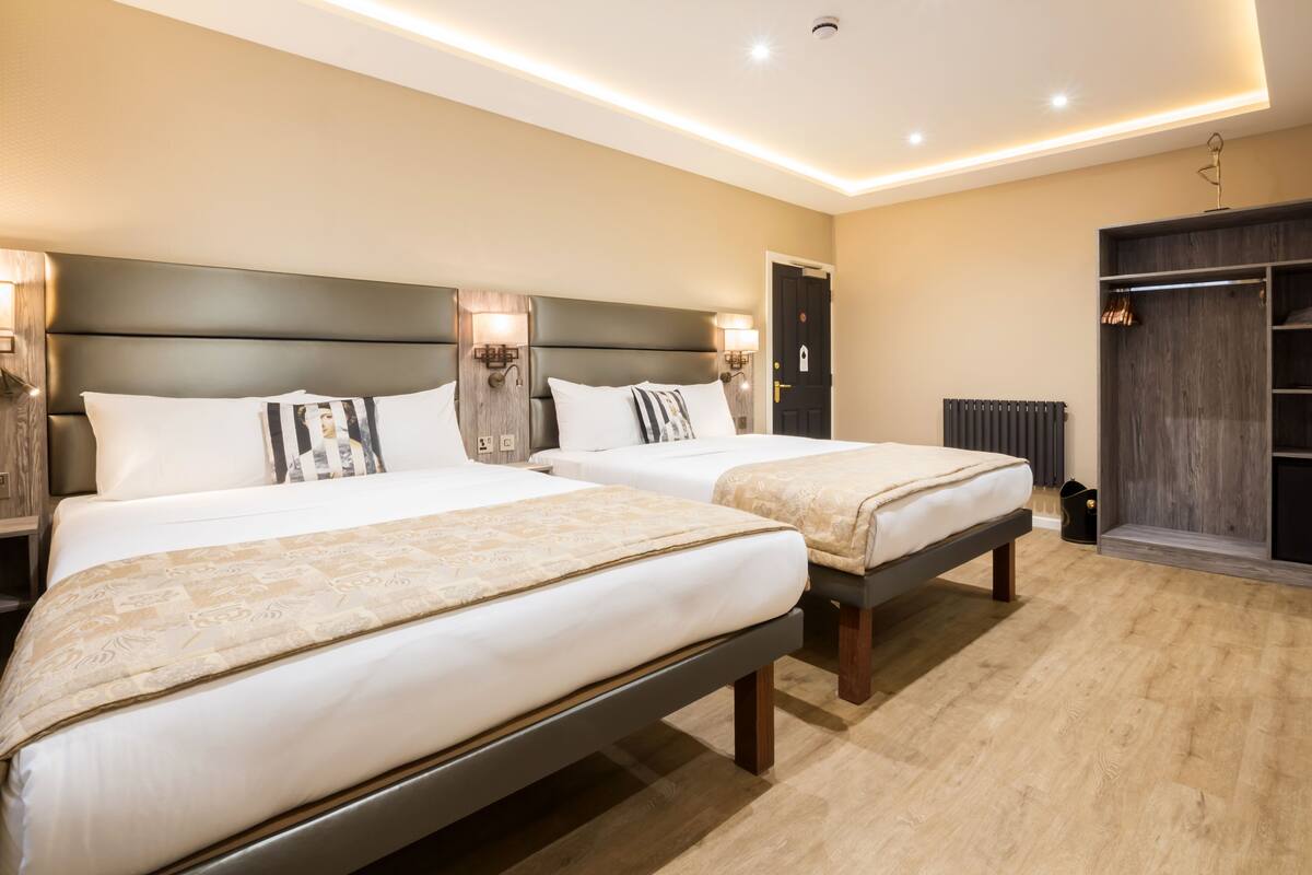 A hotel room with two beds, a wardrobe, and a radiator.